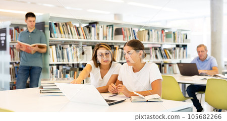 Two friendly adult female students studying in university library, using books and laptop while preparing for lecture 105682266
