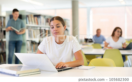 Concentrated young woman checking planner while studying and using laptop in the library 105682300
