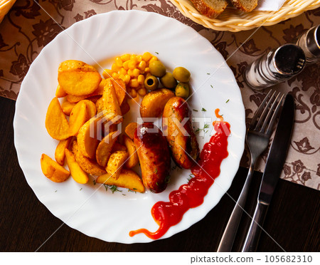 Grilled sausages served with potatoes, olives and chili sauce Grilled sausages served with potatoes, olives and chili sauce 105682310