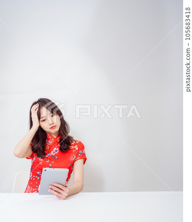 Beautiful asian woman wearing traditional cheongsam qipao dress suffering from headache desperate after using tablet on white background. 105683418