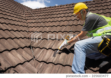 Worker man using silicone sealant adhesive to fix crack of the old tile roof. Worker man using silicone sealant adhesive to fix crack of the old tile roof. 105683477
