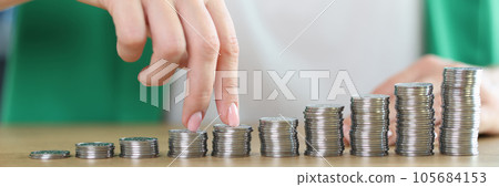 Women's fingers move over growing stacks of coins on table close-up. 105684153