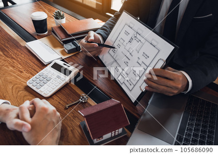 Agents are using pens pointing to blueprint home design and are being explained to customers at the office. Agents are using pens pointing to blueprint home design and are being explained to customers at the office. 105686090
