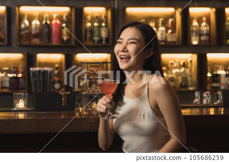 Asian woman drinking a cocktail at a bar at night. Asian woman drinking a cocktail at a bar at night. 105686259