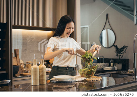 Asian housewife preparing fresh vegetables to make salad at home kitchen counter. Asian housewife preparing fresh vegetables to make salad at home kitchen counter. 105686276