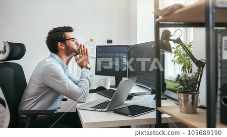 Important moment. Worried young businessman or trader in formalwear keeping palms together and looking at trading charts and financial data while working in the office. Important moment. Worried young businessman or trader in formalwear keeping palms together and looking at trading charts and financial data while working in the office. 105689190