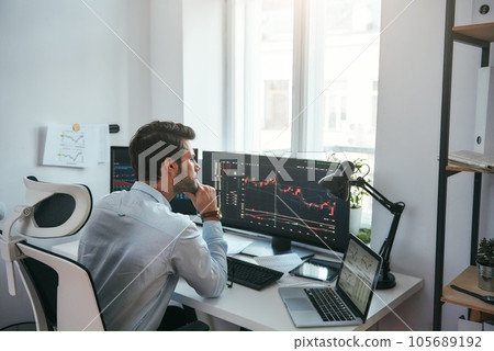Trading on world markets. Young stock market broker analyzing data and graphs on multiple computer screens while sitting in modern office 105689192
