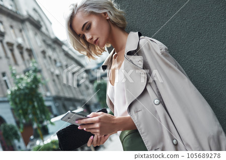 Fashion. Young stylish woman standing on the city street using application on smartphone concentrated close-up 105689278