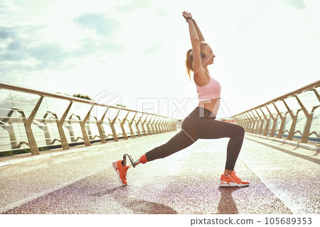 Morning yoga. Full-length of young disabled woman with leg prosthesis in sportswear doing yoga exercises while standing on the bridge 105689353