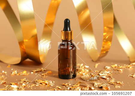cosmetic serum essence oil bottle with pipette, golden ribbons, pieces of golden paper on gold background. cosmetology beauty product for facial care, mockup, template 105691207
