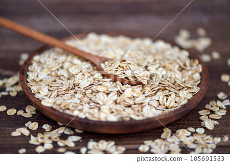 Oat flakes uncooked in wooden bowl with spoon on a dark wooden table. Concept of healthy eating 105691583