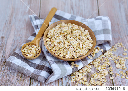 Oat flakes uncooked in wooden bowl with spoon on rustic table. Concept of healthy eating Oat flakes uncooked in wooden bowl with spoon on rustic table. Concept of healthy eating 105691648