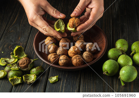 Cleaning nuts from green skins by the hands of a cook after harvesting. Working environment on the kitchen table. Cleaning nuts from green skins by the hands of a cook after harvesting. Working environment on the kitchen table. 105691960