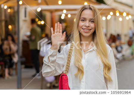 Young woman smiling friendly at camera, waving hands hello, hi, greeting or goodbye in city street Young woman smiling friendly at camera, waving hands hello, hi, greeting or goodbye in city street 105691964