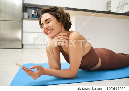 Fitness and technology. Smiling brunette woman in activewear, workout at home, looking at smartphone with happy face, watching training instructor on mobile phone app 105693021