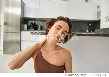 Close up portrait of sportswoman, fitness woman massaging her neck, warm-up her body after workout, doing yoga on rubber mat at home 105693161