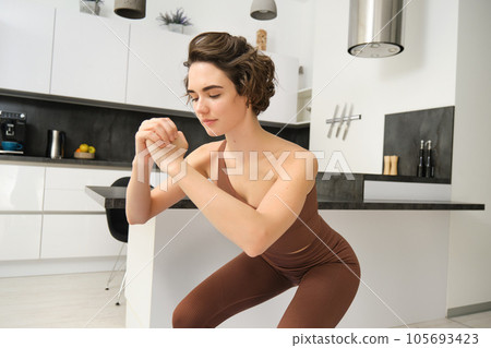 Workout and women wellbeing concept. Young fitness woman, doing squats, workout from home without gym equipment, training in bright room 105693423