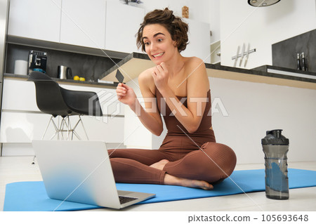 Portrait of young female athlete, yoga girl paying for online classes, purchasing remote training with gym instructor, sitting on her rubber mat with laptop and credit card Portrait of young female athlete, yoga girl paying for online classes, purchasing remote training with gym instructor, sitting on her rubber mat with laptop and credit card 105693648