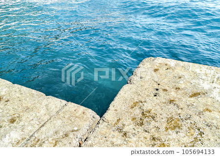Grey concrete pier at blue sea water with small waves Grey concrete pier at blue sea water with small waves 105694133