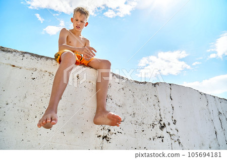 Preteen boy sits on sunny pier watching seaside against sky 105694181