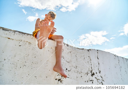 Preteen boy smiling happily on high pier raises leg up 105694182