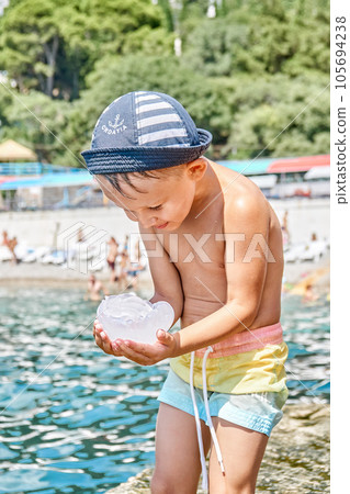 Preschooler boy standing on stone pier holds big jellyfish 105694238