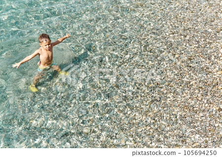 Preschooler boy enjoys exploring sea water at pebble beach 105694250