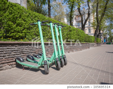[Ukraine] Four yellow-green electric scooters parked on a cobbled sidewalk in the capital Kyiv 105695314