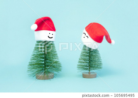 Two small Christmas trees in a red Santa Hats. Decorating of Artificial Fir tree. Beautiful imitation of a mini Christmas tree, with Santa Cap on blue background. Christmas holidays concept Two small Christmas trees in a red Santa Hats. Decorating of Artificial Fir tree. Beautiful imitation of a mini Christmas tree, with Santa Cap on blue background. Christmas holidays concept 105695495