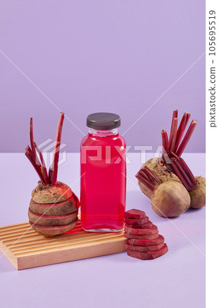 Unlabeled glass bottle of pink juice decorated with stacks of many beetroot round slices. Purple background. Branding mockup with empty label bottle Unlabeled glass bottle of pink juice decorated with stacks of many beetroot round slices. Purple background. Branding mockup with empty label bottle 105695519