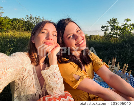 Two friends take a selfie on a blue blanket for an outdoor picnic Two friends take a selfie on a blue blanket for an outdoor picnic 105696040
