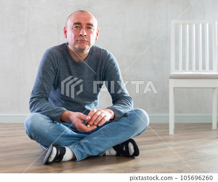 Middle-aged man in casual clothes sitting on the floor in the living room 105696260