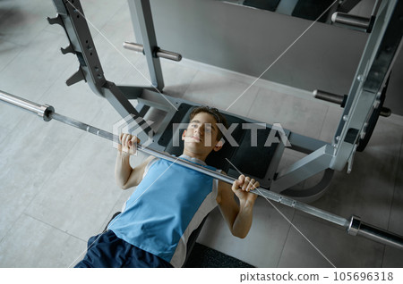Serious skinny guy raising heavy barbell rod pipe at gym Serious skinny guy raising heavy barbell rod pipe at gym 105696318