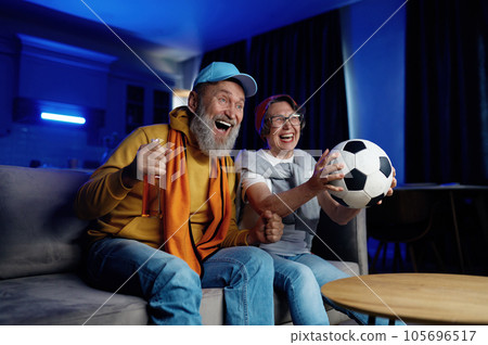 Expressive senior family couple watching football match on tv at home 105696517