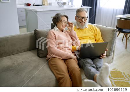 Elderly couple using laptop together and sitting on couch at home Elderly couple using laptop together and sitting on couch at home 105696539