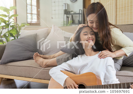 LGBTQIA lesbian gay couple playing guitar and singing with romantic feelings at home 105697691