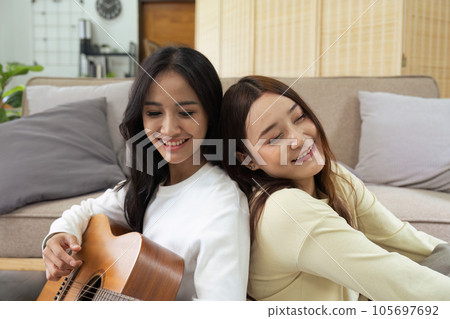 LGBTQIA lesbian gay couple playing guitar and singing with romantic feelings at home LGBTQIA lesbian gay couple playing guitar and singing with romantic feelings at home 105697692