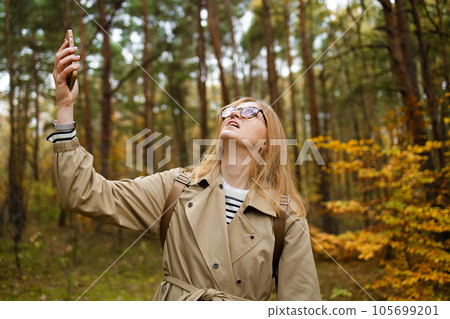 Woman searching for the mobile coverage on the mobile phone stands in a autumn forest, no service screen Woman searching for the mobile coverage on the mobile phone stands in a autumn forest, no service screen 105699201
