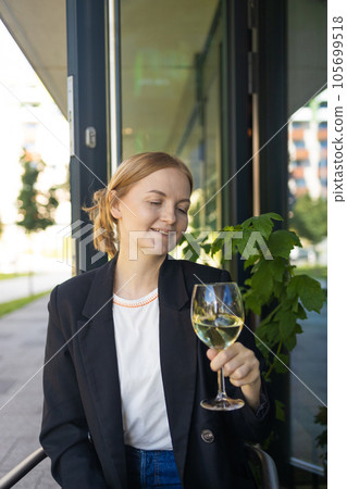 Woman drinking white wine from a glass at city cafe. Beautiful female enjoying cozy evening on terrace. Summertime relax at sunny patio. Woman drinking white wine from a glass at city cafe. Beautiful female enjoying cozy evening on terrace. Summertime relax at sunny patio. 105699518