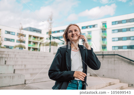Portrait of corporate woman answers phone call while walking to the office building.  105699543