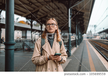 Angry lost woman waiting on the station platform and using smart phone at the airport link station, Gdansk, Poland. Angry lost woman waiting on the station platform and using smart phone at the airport link station, Gdansk, Poland. 105699559