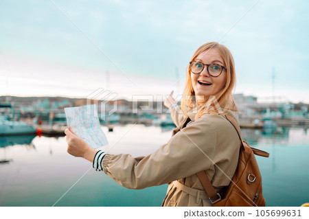 Happy traveler woman with a map and backpack on a lake pier, feeling freedom and enjoying. Travel around Europe. High quality photo 105699631