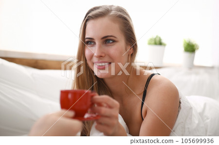 blond woman have cup of tea coffee early morning in her bed 105699936