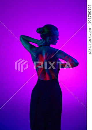 Back view. Tender relaxing woman in digital neon filter lights showing red flower on back over gradient purple background. 105700103
