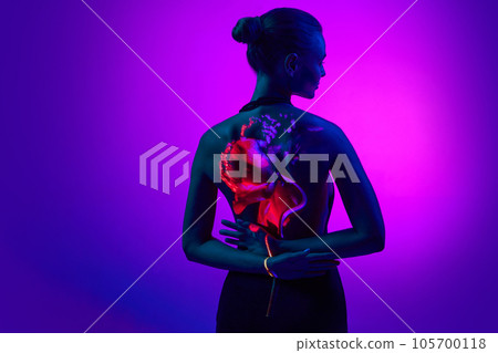 Back view. Portrait with sensual female silhouette and digital neon filter lights with flower on back and hands over gradient purple background. Back view. Portrait with sensual female silhouette and digital neon filter lights with flower on back and hands over gradient purple background. 105700118