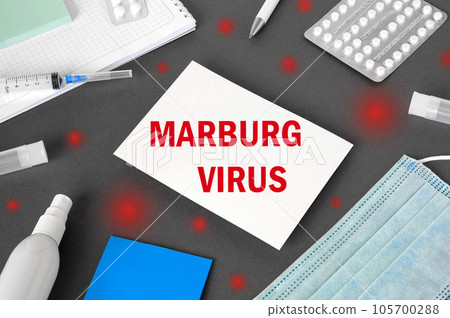 The word Marburgvirus on Gray modern doctor desk table background. Mask, notepad, syringe, sanitizer and supplies. MARV, Marburg Virus spreading. Medicine and healthcare, medical education. Top view 105700288