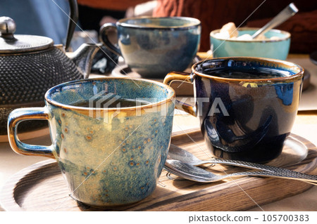 Brewing and Serving Tea. Teapot Poured Green Tea Blue Ceramic Cup on Wooden Cafe Table. Two Pottery Handmade Mugs Early in the Morning. Trendy Authentic Porcelain Set. Breakfast Concept. Tea Time Brewing and Serving Tea. Teapot Poured Green Tea Blue Ceramic Cup on Wooden Cafe Table. Two Pottery Handmade Mugs Early in the Morning. Trendy Authentic Porcelain Set. Breakfast Concept. Tea Time 105700383