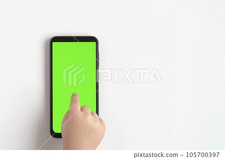 Child hand touching clicking on mobile phone with chromakey screen. Little Baby Finger Taps in the center of blank phone green display. Close up. Using smartphone device. Top view Flat lay 105700397