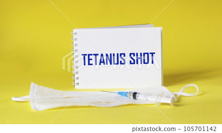tetanus shot text is written on a notepad and a yellow background, next to a medical mask tetanus shot text is written on a notepad and a yellow background, next to a medical mask 105701142