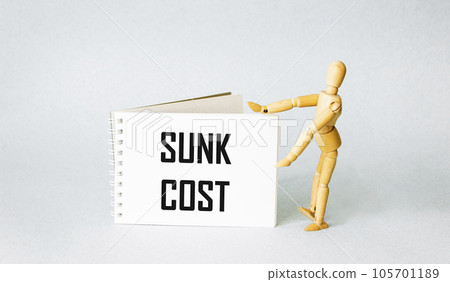Notepad with the text sunk cost and a wooden doll on a light background 105701189
